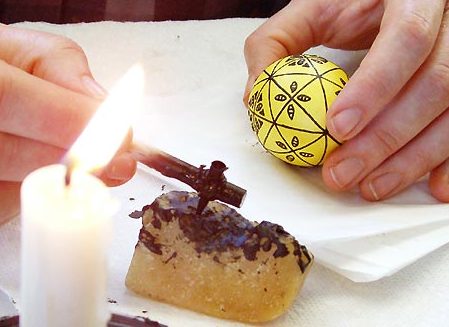 handing holding a yellow egg being dyed with wax