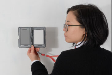 portrait of an asian woman wearing glasses looking to the left towards a device in her hand with gray tones