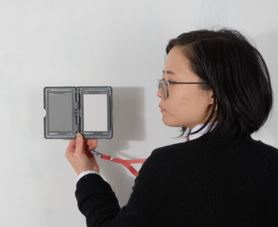 portrait of an asian woman wearing glasses looking to the left towards a device in her hand with gray tones